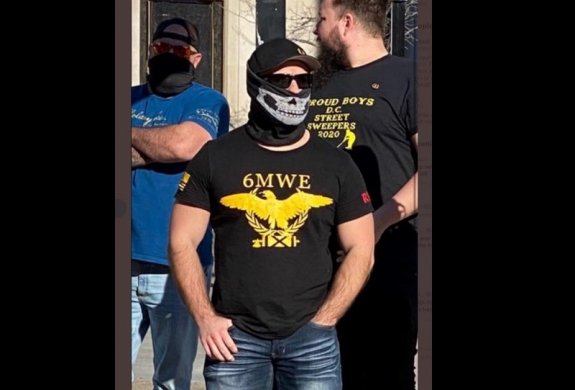 A photograph of three men. One wears a black t-shirt bearing the text "Proud Boys: D.C. Street Sweepers 2020." Another, in front of him, wears a t-shirt with the text "6MWE" over an image of an eagle holding a fasces in a laurel wreath.